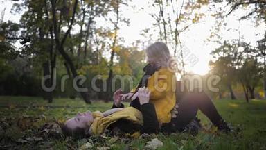 快乐的童年，一位年轻的母亲和一个可爱的女儿在公园的秋草甸里玩得开心，躺在草坪上，<strong>落叶飘</strong>落